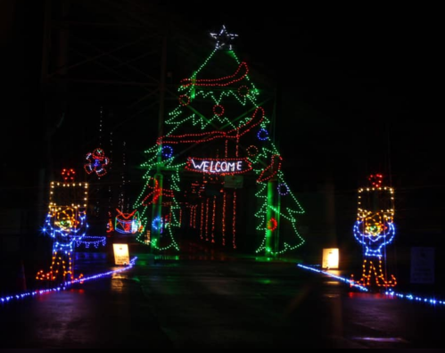 A brightly lit Christmas tree archway with colorful lights and festive decorations, welcoming visitors at night.