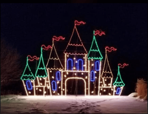 A brightly lit castle made of colorful Christmas lights, featuring multiple towers and flags, set against a dark night sky.