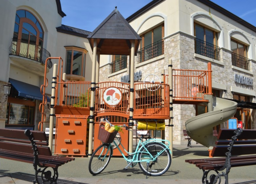 A colorful playground with a slide and climbing structure, alongside a vintage bicycle parked on a sunny day.