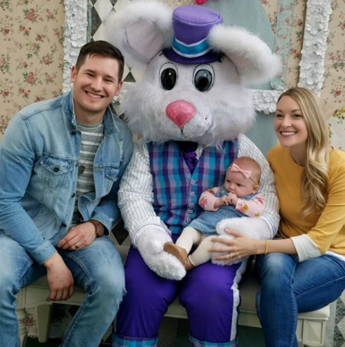 A family poses with a large, costumed Easter bunny, smiling with a baby in their lap.