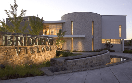 Modern building exterior with stone signage reading "Bridgeport Village," surrounded by landscaping at dusk.