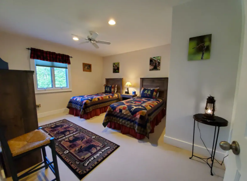 Cozy bedroom with two twin beds, a rug, a nightstand, and nature-themed decor. Soft lighting and a window view.