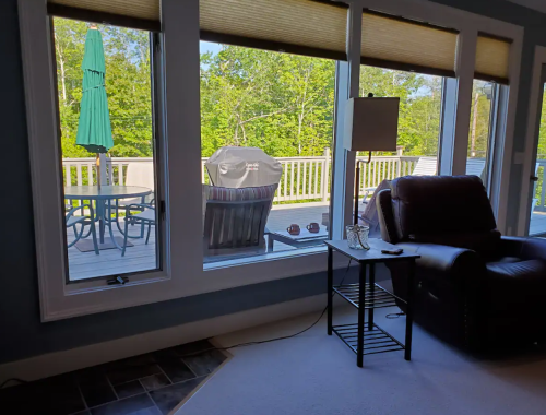 A cozy living room with a view of a deck, featuring a green umbrella, chairs, and a lamp beside a recliner.