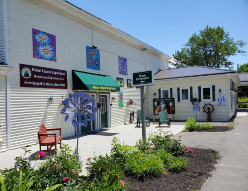 Exterior of the Maine Alpaca Experience building, featuring colorful flower murals and a welcoming entrance sign.