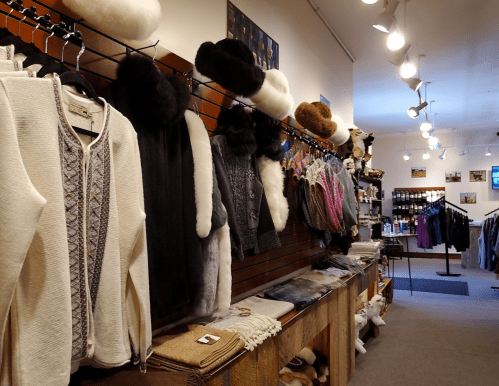 A cozy store display featuring various clothing items, including sweaters, hats, and scarves, on wooden shelves.