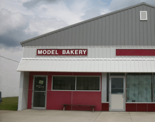 Exterior of Model Bakery, featuring a red and gray building with a sign above the entrance. Cloudy sky in the background.