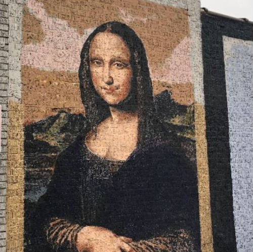 Mural of the Mona Lisa on a textured wall, blending classic art with urban street style.