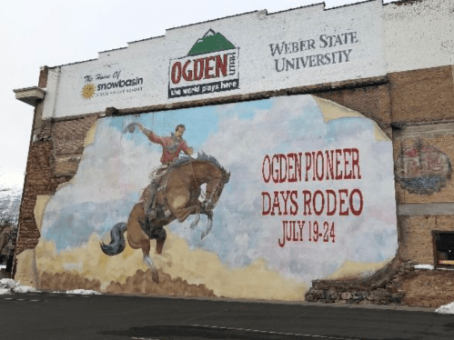 Mural of a cowboy riding a horse, promoting Ogden Pioneer Days Rodeo, July 19-24, on a building in Ogden, Utah.