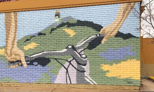 Mural of hands gripping a bicycle handlebar with a colorful landscape in the background.