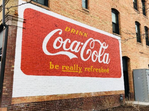Vintage Coca-Cola mural on a brick wall, featuring the slogan "Drink Coca-Cola, be really refreshed."