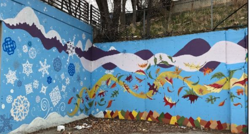 Colorful mural featuring snowflakes, waves, and autumn leaves on a blue background, set against a natural landscape.