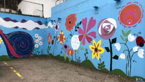 Colorful mural featuring flowers, a snail, and whimsical designs on a blue wall in an outdoor setting.