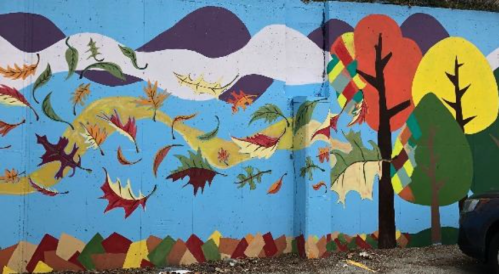 Colorful mural featuring trees, leaves, and mountains against a blue sky, capturing a vibrant autumn scene.