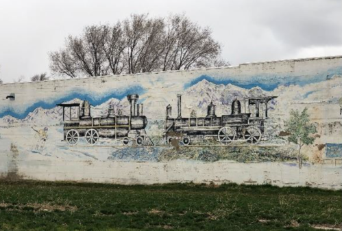 Mural of two vintage steam locomotives on a wall, set against a backdrop of mountains and trees.