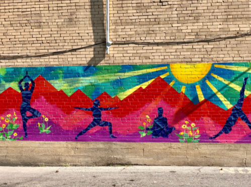 Colorful mural featuring silhouettes of people practicing yoga against a vibrant mountain and sun backdrop.