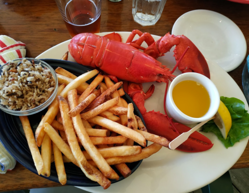 A plate featuring a cooked lobster, fries, rice, a small bowl of melted butter, and a lemon wedge.