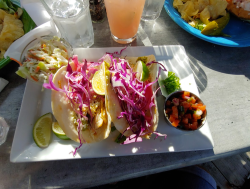 Two fish tacos topped with purple cabbage and lime, served with a side of pico de gallo and a salad.
