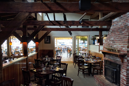 Cozy restaurant interior with wooden beams, tables set for dining, and a view of an outdoor patio.