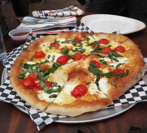 A freshly baked pizza topped with cherry tomatoes and basil on a checkered paper, served on a metal plate.