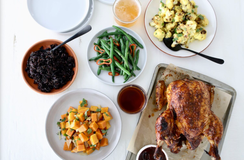 A spread of roasted chicken, black rice, green beans, cauliflower, and butternut squash on a white table.