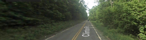 A quiet, tree-lined road labeled Clinton Rd, with greenery on both sides and a faint mist in the distance.