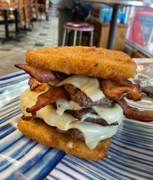 A stacked sandwich featuring crispy bacon, melted cheese, and beef patties, all between two golden, fried layers.