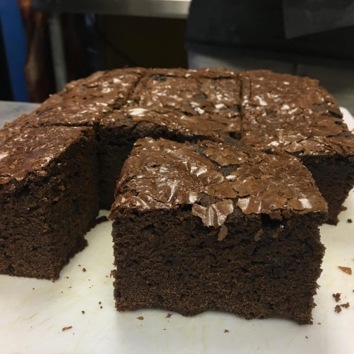 A close-up of freshly baked chocolate brownies, cut into squares, on a white cutting board.