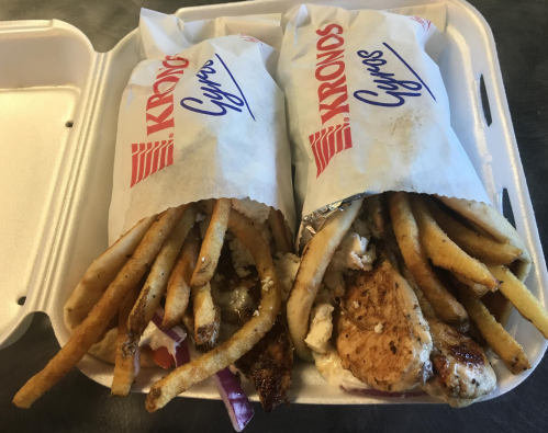 Two gyros wrapped in paper, filled with grilled chicken, fries, and vegetables, served in a takeout container.
