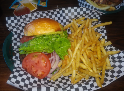 A juicy burger with lettuce, tomato, and onion, served with a side of golden French fries on a checkered paper.