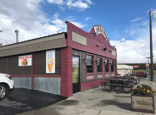 Exterior of Wild Bill's restaurant with a colorful sign, picnic tables outside, and a cloudy sky in the background.