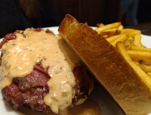 A close-up of a sandwich with meat and sauce, served with a side of golden French fries on a white plate.