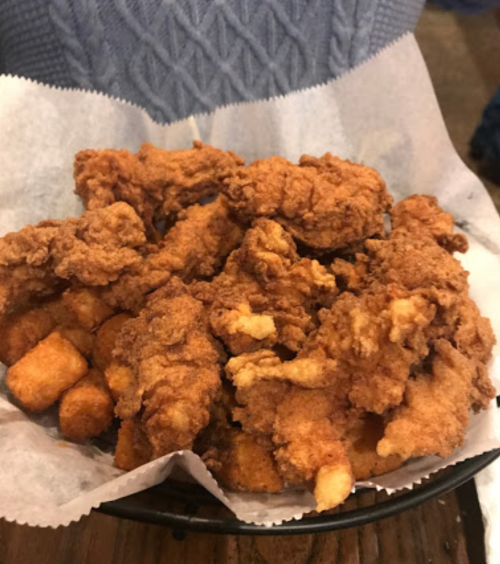 A basket of crispy fried chicken pieces served with golden tater tots on a bed of parchment paper.