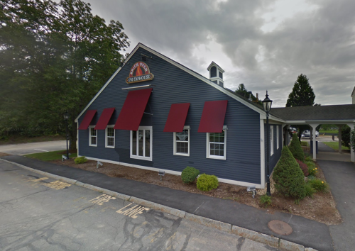A blue building with red awnings and a sign, surrounded by greenery and a cloudy sky.