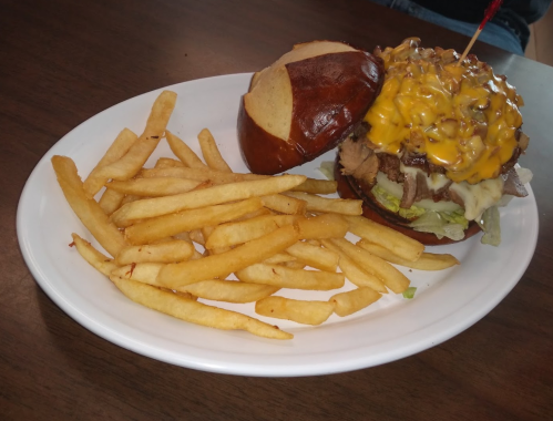 A pretzel bun burger topped with melted cheese and onions, served with a side of golden French fries on a white plate.