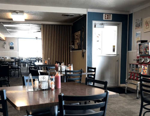 Interior of a casual diner with empty tables, condiments on the table, and an exit door in the background.