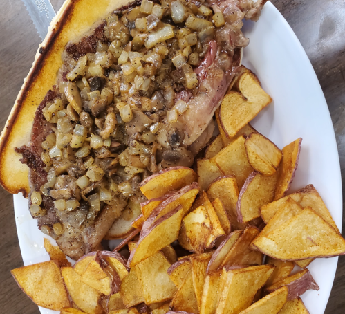 A plate featuring a large steak topped with sautéed onions and mushrooms, served with crispy potato wedges.