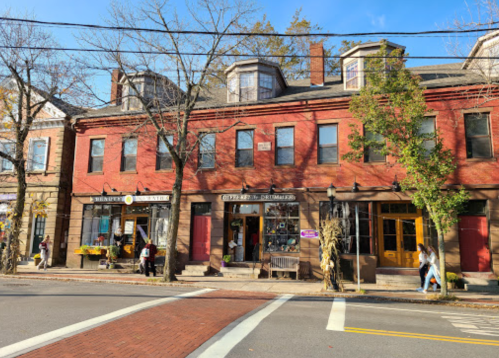 A charming red brick building with shops, surrounded by trees and pedestrians on a sunny day.