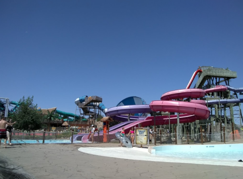 A water park featuring colorful slides, a lazy river, and a clear blue sky. People enjoy the attractions.