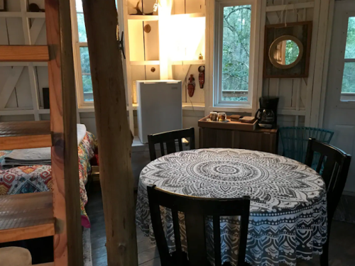 Cozy interior of a cabin featuring a round table, kitchenette, and large windows with natural light.