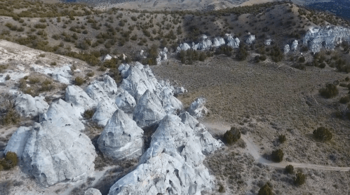 Aerial view of unique white rock formations surrounded by sparse vegetation and rolling hills.