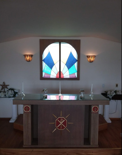 A simple church altar with a stained glass window and candles, surrounded by decorative elements.