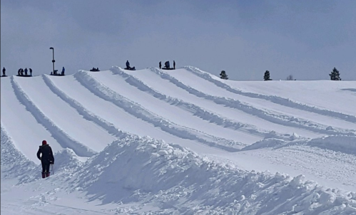 A snowy landscape with layered snow hills and people enjoying winter activities in the background.