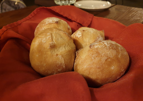 A basket lined with a red cloth containing four freshly baked bread rolls.