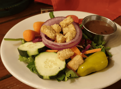 A fresh salad with mixed greens, cucumbers, carrots, red onion, croutons, and a side of dressing.