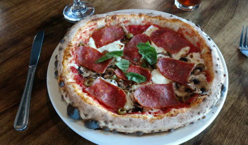 A delicious pizza topped with pepperoni, mozzarella, mushrooms, olives, and fresh basil on a wooden table.