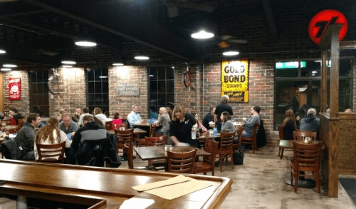 A bustling restaurant interior with diners at wooden tables, exposed brick walls, and vintage decor.