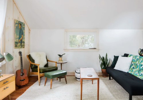 Cozy living space with a green chair, guitar, plants, and a black sofa, featuring natural light and wooden accents.