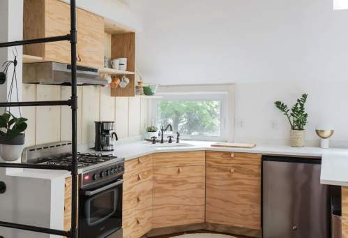 Modern kitchen with wooden cabinets, a gas stove, coffee maker, and a window with greenery outside.