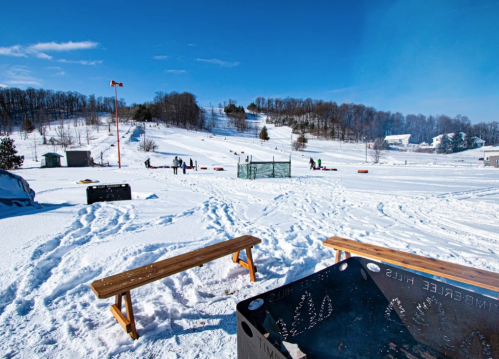 A snowy landscape with ski slopes, benches, and people enjoying winter activities under a clear blue sky.