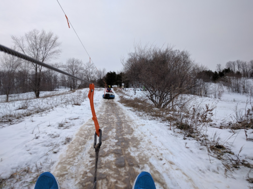A view from a snow tubing ride, showing a snowy path and trees in the background.